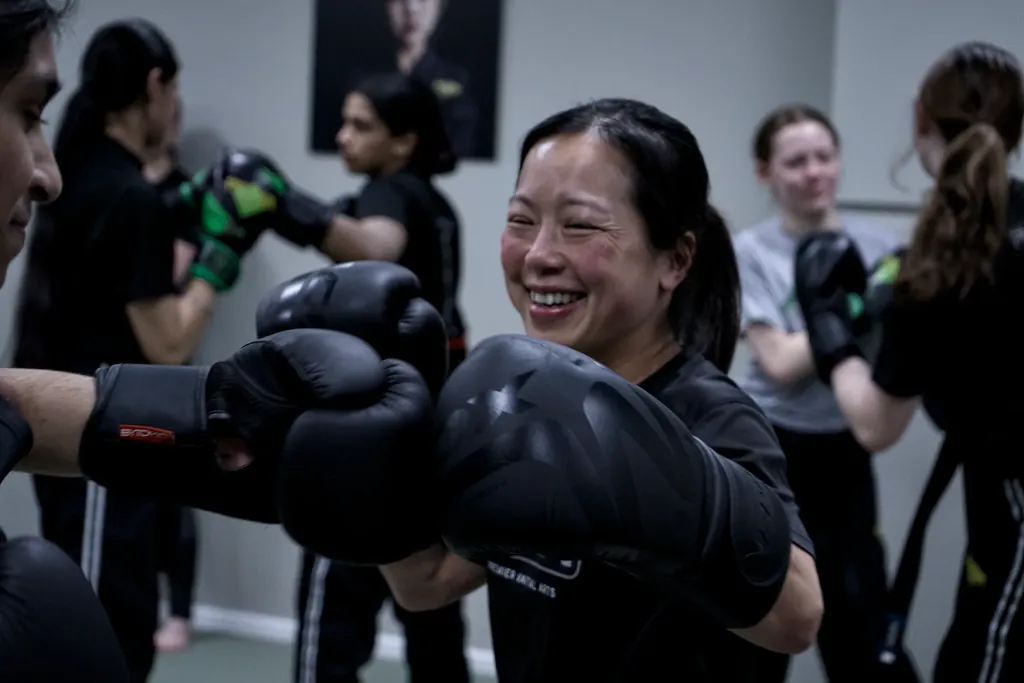 An adult student smiling while working combinations in boxing gloves