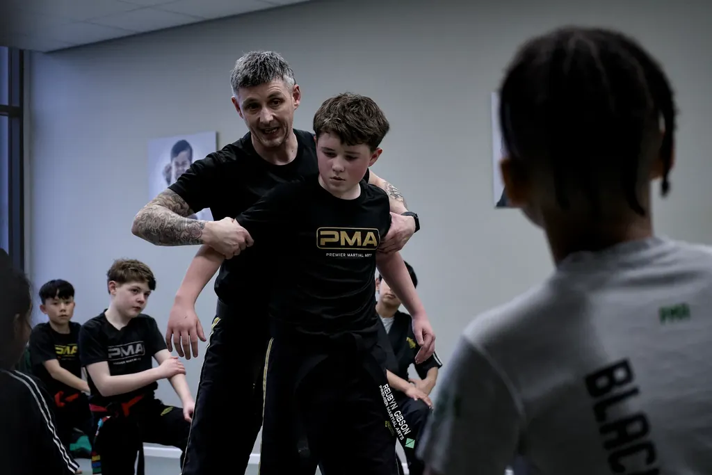 An instructor guiding a boy through a technique while the class watches